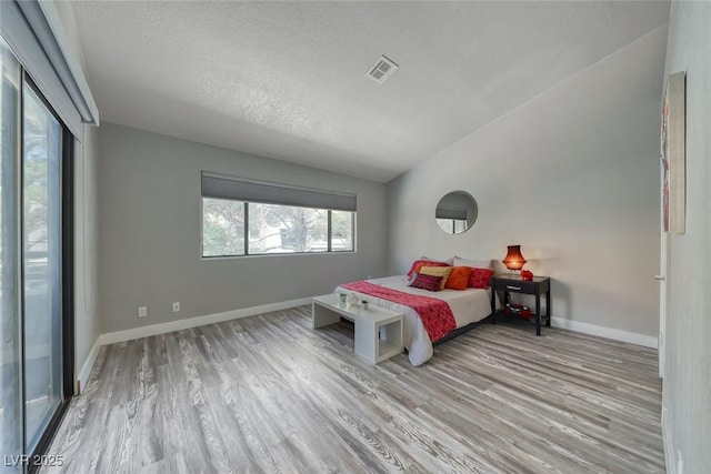 bedroom featuring wood finished floors, a textured ceiling, lofted ceiling, and baseboards