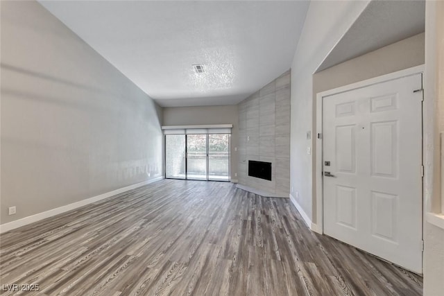 unfurnished living room with wood finished floors, baseboards, a textured ceiling, and a fireplace