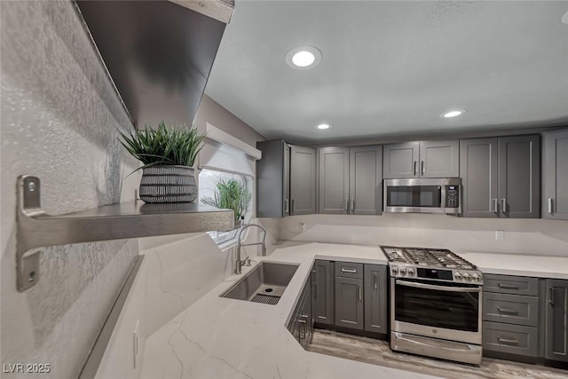 kitchen with stainless steel appliances, a sink, gray cabinetry, light stone countertops, and recessed lighting