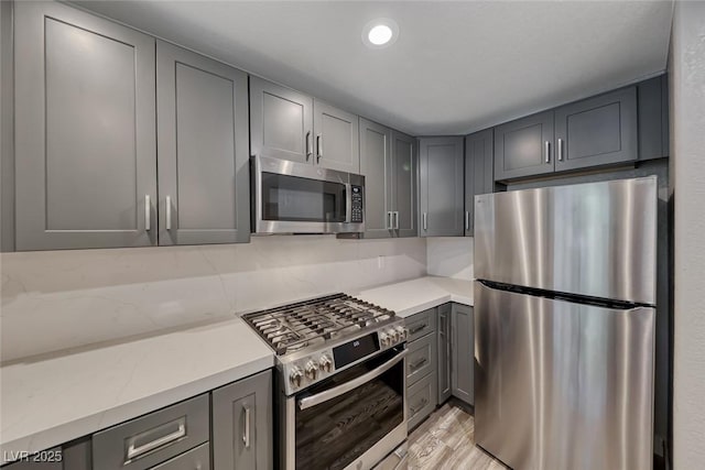 kitchen featuring appliances with stainless steel finishes, gray cabinetry, light wood-type flooring, and light stone counters
