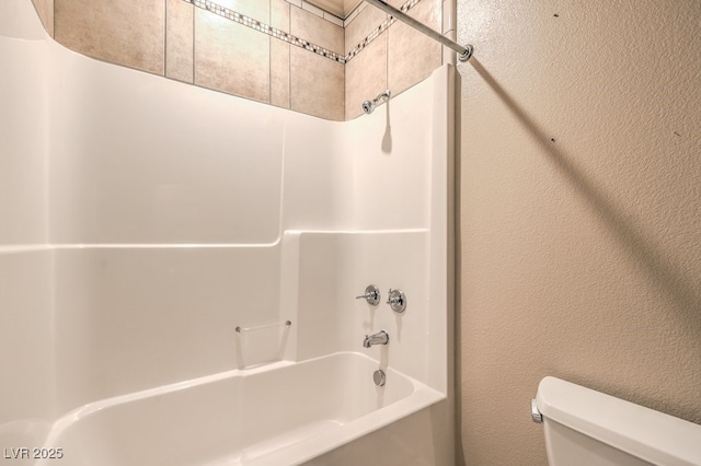 bathroom with toilet, shower / bath combination, and a textured wall