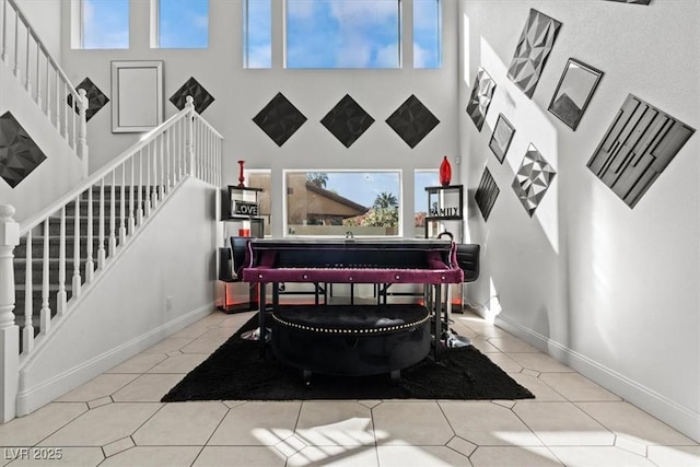sitting room with a towering ceiling, plenty of natural light, stairway, tile patterned floors, and baseboards