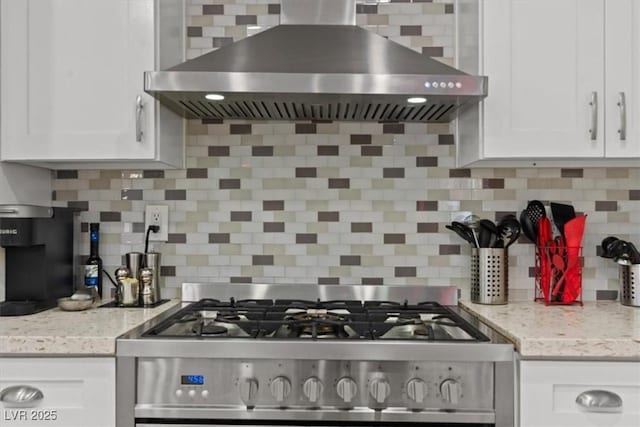 kitchen featuring stainless steel gas stove, wall chimney range hood, tasteful backsplash, white cabinetry, and light stone counters