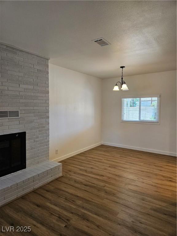 unfurnished living room with dark wood finished floors, baseboards, a chandelier, a brick fireplace, and a textured ceiling