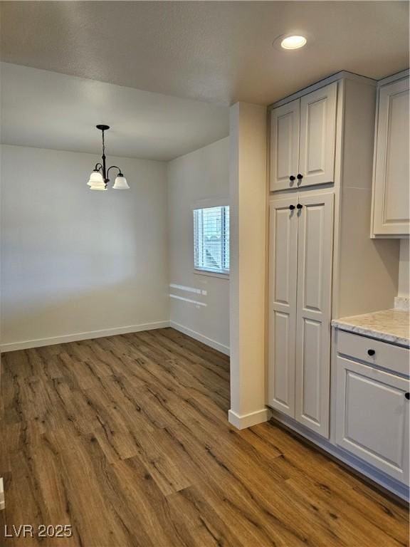 unfurnished dining area featuring wood finished floors, a chandelier, baseboards, and recessed lighting
