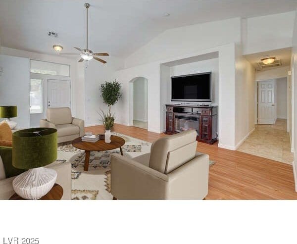 living room with arched walkways, lofted ceiling, ceiling fan, and light wood-style floors