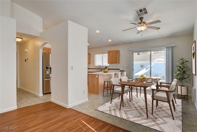dining space featuring arched walkways, a ceiling fan, light wood finished floors, baseboards, and recessed lighting