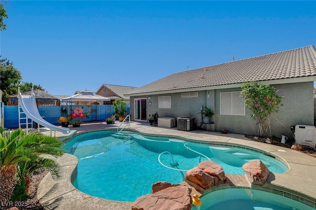 view of swimming pool with a water slide, cooling unit, a fenced backyard, and a pool with connected hot tub