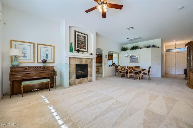 living area featuring carpet floors, a ceiling fan, arched walkways, and a tile fireplace