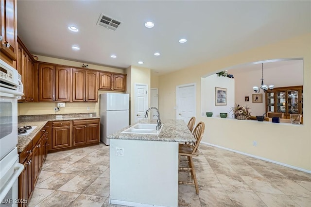 kitchen featuring white appliances, a sink, a chandelier, light stone countertops, and brown cabinets