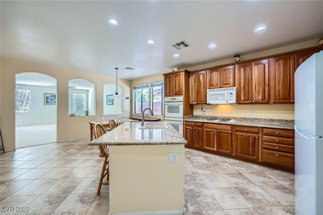 kitchen with white appliances, a sink, arched walkways, light stone counters, and brown cabinets