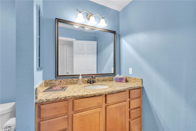 bathroom featuring toilet, vanity, and a textured wall