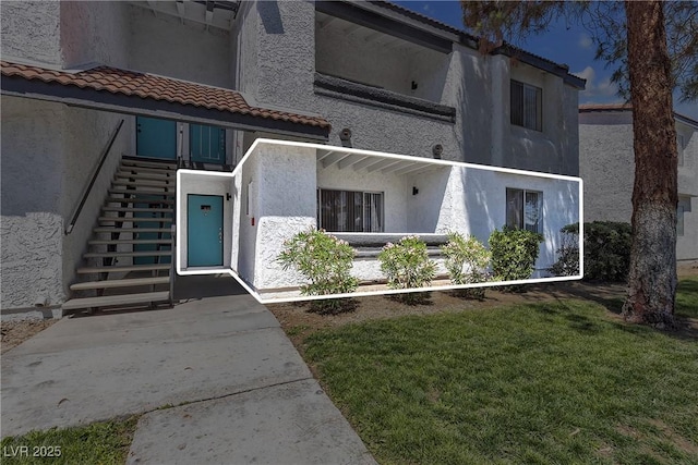 view of front of home with a tiled roof, stucco siding, stairs, and a front yard