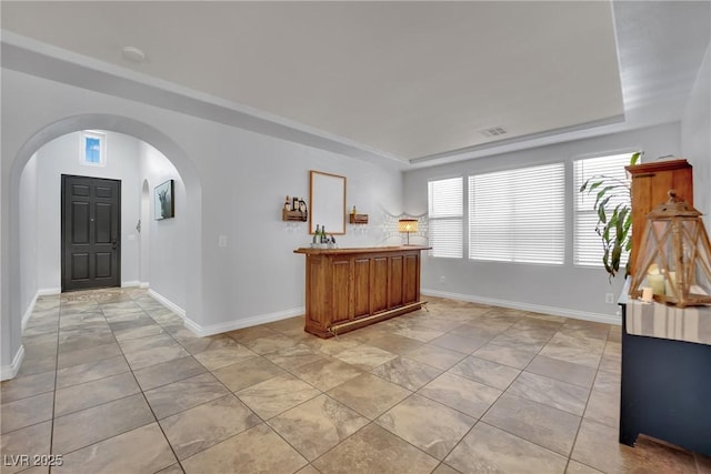 foyer with arched walkways, baseboards, a tray ceiling, and light tile patterned floors