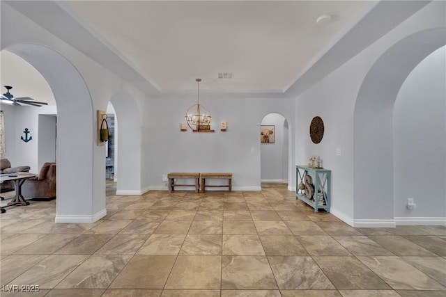 dining space with a raised ceiling, a ceiling fan, arched walkways, a chandelier, and baseboards
