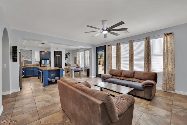 living area featuring ceiling fan, baseboards, and arched walkways