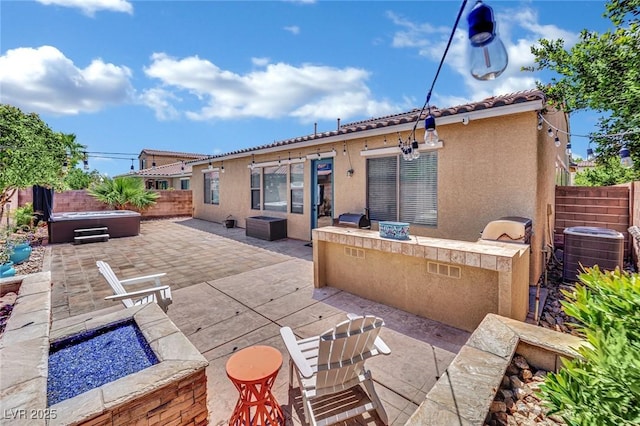 rear view of property featuring a hot tub, central AC unit, a patio, a fenced backyard, and an outdoor kitchen