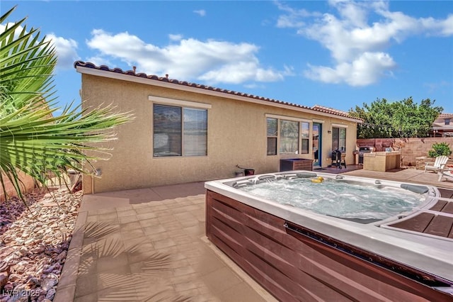 rear view of house with a hot tub, stucco siding, a patio area, and a tile roof