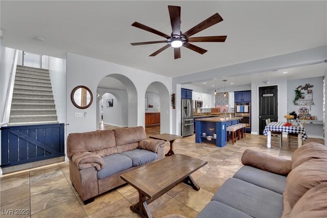 living room featuring a ceiling fan, arched walkways, and stairs