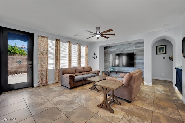 living room with ceiling fan, baseboards, and arched walkways