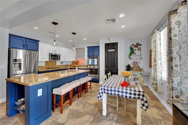 kitchen featuring stainless steel appliances, blue cabinetry, a kitchen bar, a sink, and light stone counters