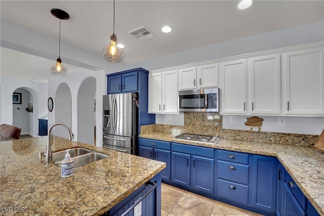 kitchen featuring appliances with stainless steel finishes, a sink, blue cabinetry, arched walkways, and white cabinets