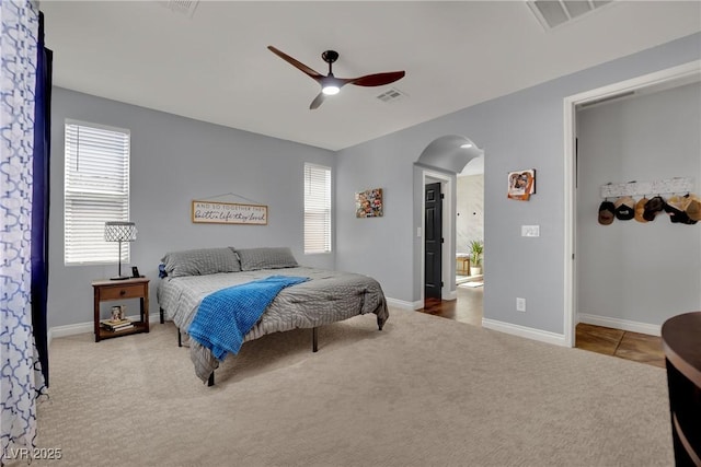carpeted bedroom featuring arched walkways, a ceiling fan, and baseboards