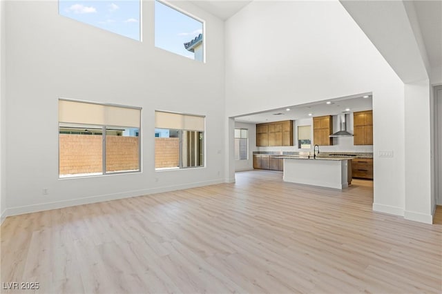 10851 Hanwicke Harbor Ave, Las Vegas, NV 89166 - unfurnished living room with light wood-type flooring, baseboards, a high ceiling, and a sink