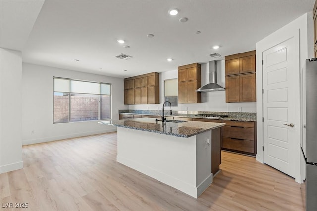 10851 Hanwicke Harbor Ave, Las Vegas, NV 89166 - kitchen featuring wall chimney exhaust hood, a sink, stainless steel gas cooktop, an island with sink, and dark stone countertops