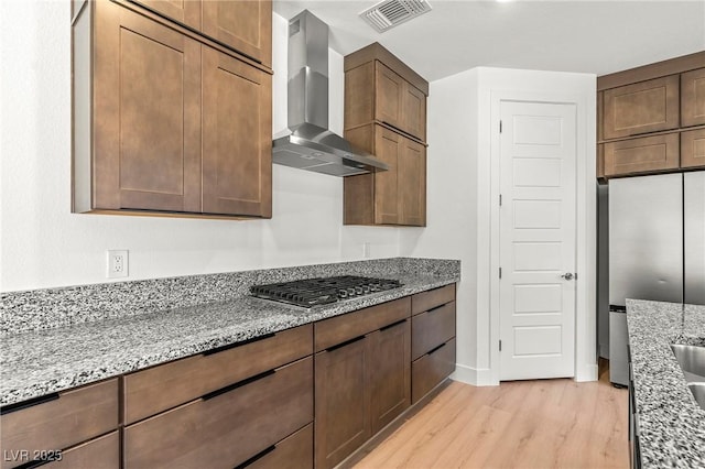 10851 Hanwicke Harbor Ave, Las Vegas, NV 89166 - kitchen featuring wall chimney exhaust hood, stainless steel appliances, light wood-style flooring, light stone counters, and baseboards