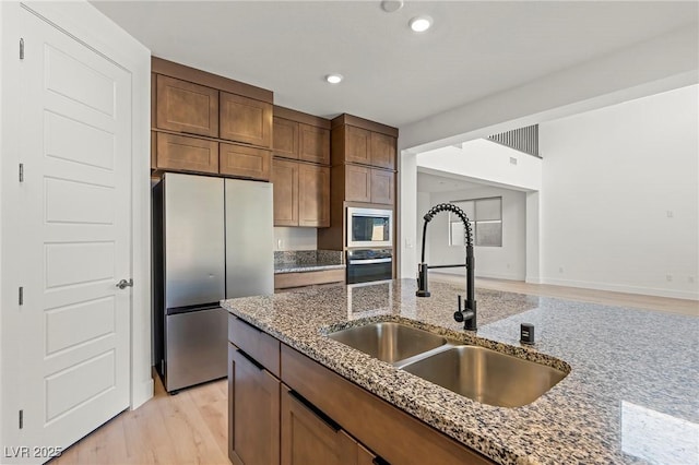 10851 Hanwicke Harbor Ave, Las Vegas, NV 89166 - kitchen featuring appliances with stainless steel finishes, a sink, stone countertops, light wood-style floors, and recessed lighting