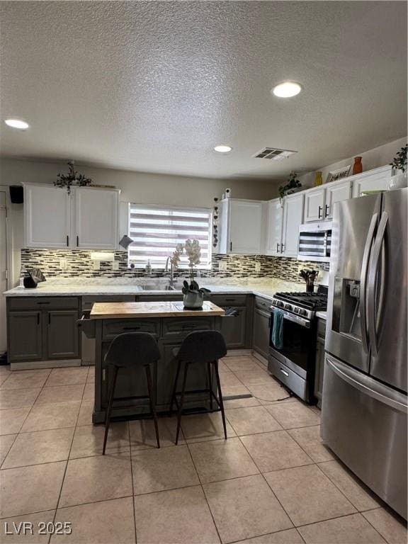 kitchen with stainless steel appliances, a sink, decorative backsplash, light countertops, and a textured ceiling