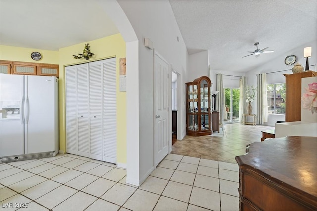 kitchen with white refrigerator with ice dispenser, arched walkways, ceiling fan, light tile patterned floors, and a textured ceiling