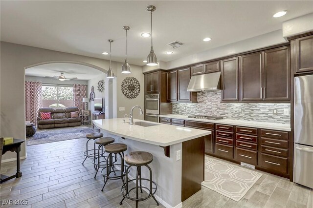 5650 Pleasant Palms St, North Las Vegas, NV 89081 - kitchen featuring under cabinet range hood, stainless steel appliances, a sink, arched walkways, and a kitchen bar