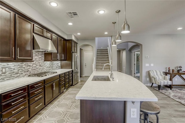 5650 Pleasant Palms St, North Las Vegas, NV 89081 - kitchen with a sink, under cabinet range hood, arched walkways, appliances with stainless steel finishes, and an island with sink