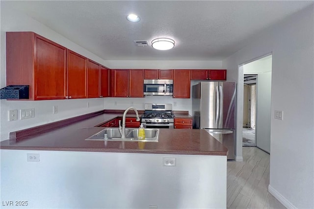 9148 Alluring Ave, Las Vegas, NV 89149 - kitchen featuring stainless steel appliances, a sink, reddish brown cabinets, a peninsula, and dark countertops