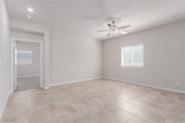 spare room with healthy amount of natural light, a ceiling fan, light tile patterned floors, and baseboards