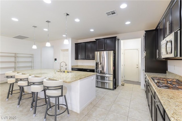 kitchen featuring appliances with stainless steel finishes, a sink, a kitchen breakfast bar, light stone counters, and an island with sink