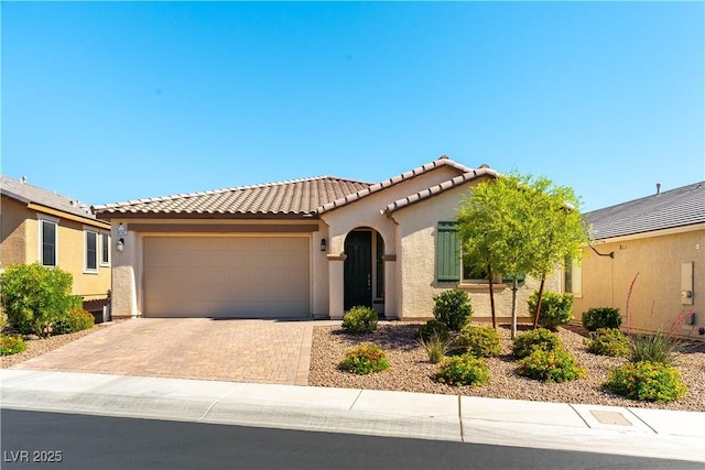 mediterranean / spanish-style home with stucco siding, an attached garage, a tiled roof, and decorative driveway