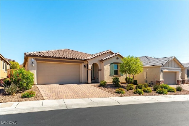 mediterranean / spanish-style home featuring an attached garage, decorative driveway, stucco siding, and a tiled roof