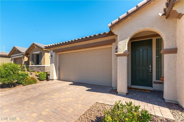property entrance featuring stucco siding, a tile roof, an attached garage, and decorative driveway