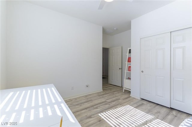unfurnished bedroom with light wood-type flooring, a closet, a ceiling fan, and baseboards
