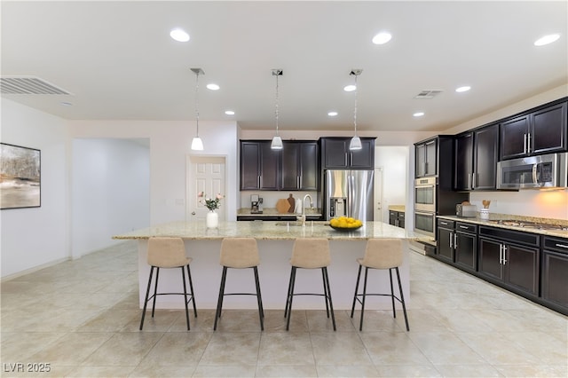 10742 Cowlite Ave, Las Vegas, NV 89166 - kitchen featuring appliances with stainless steel finishes, a kitchen island with sink, a breakfast bar, light stone countertops, and recessed lighting