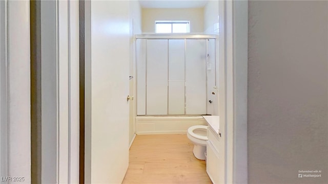 bathroom with wood finished floors, toilet, bath / shower combo with glass door, and vanity