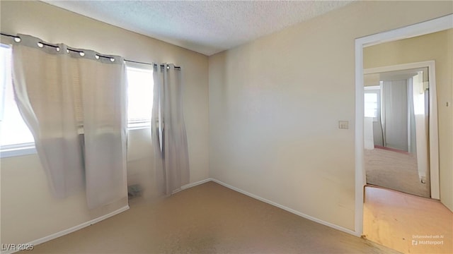 empty room featuring a textured ceiling, baseboards, and carpet