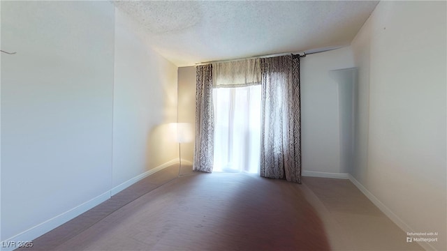 unfurnished room with baseboards and a textured ceiling