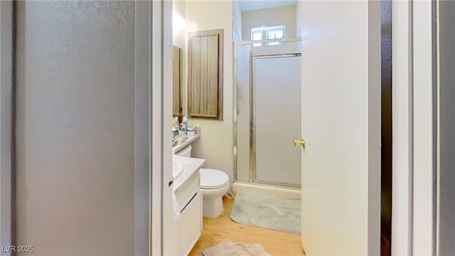 full bath with toilet, vanity, a stall shower, and wood finished floors