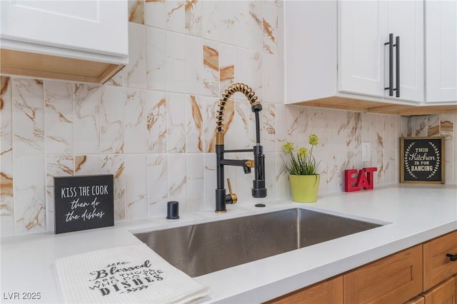 kitchen with a sink, decorative backsplash, light countertops, and white cabinetry