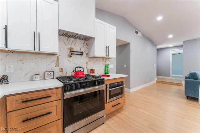 kitchen featuring stainless steel appliances, light countertops, light wood-style floors, decorative backsplash, and lofted ceiling