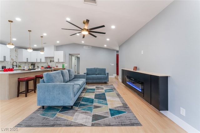 living room with lofted ceiling, light wood-style floors, a ceiling fan, baseboards, and recessed lighting